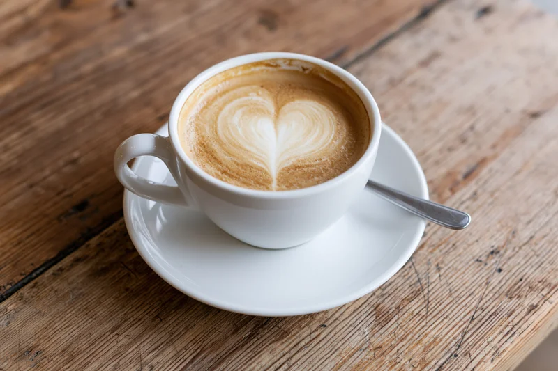 White ceramic cup of latte with heart latte art on wooden table
