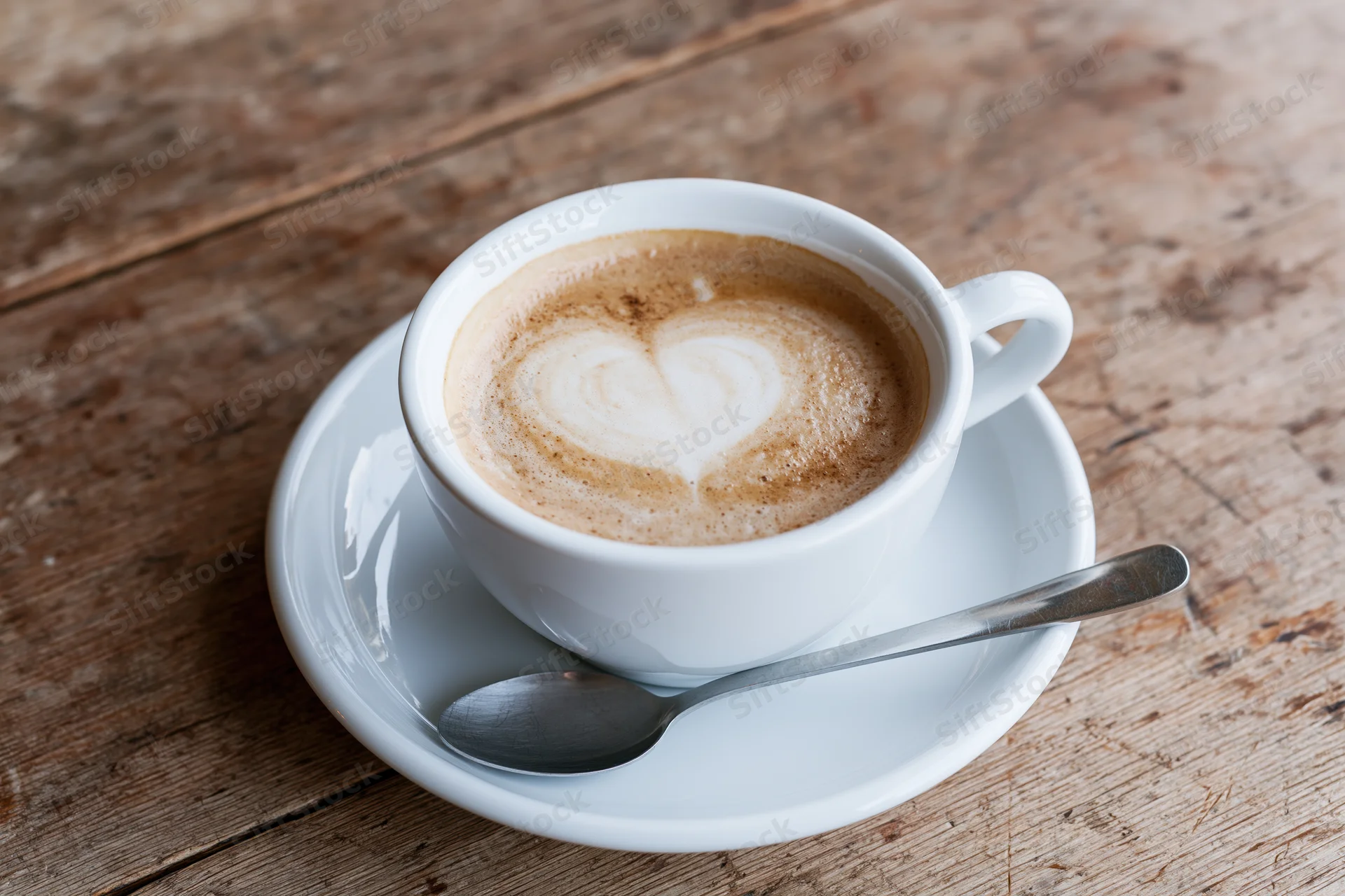 White ceramic cup of latte with heart-shaped foam art on a rustic wooden table