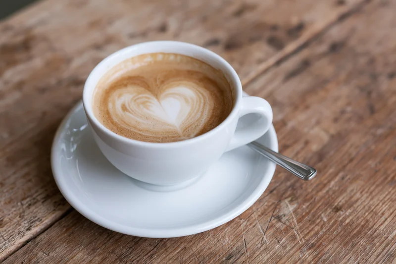 White ceramic cup of latte with heart-shaped foam art on a wooden table