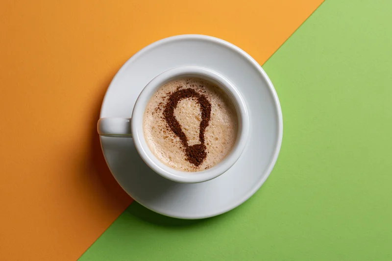 White ceramic espresso cup with cocoa-dusted lightbulb shape in foam on orange and green background