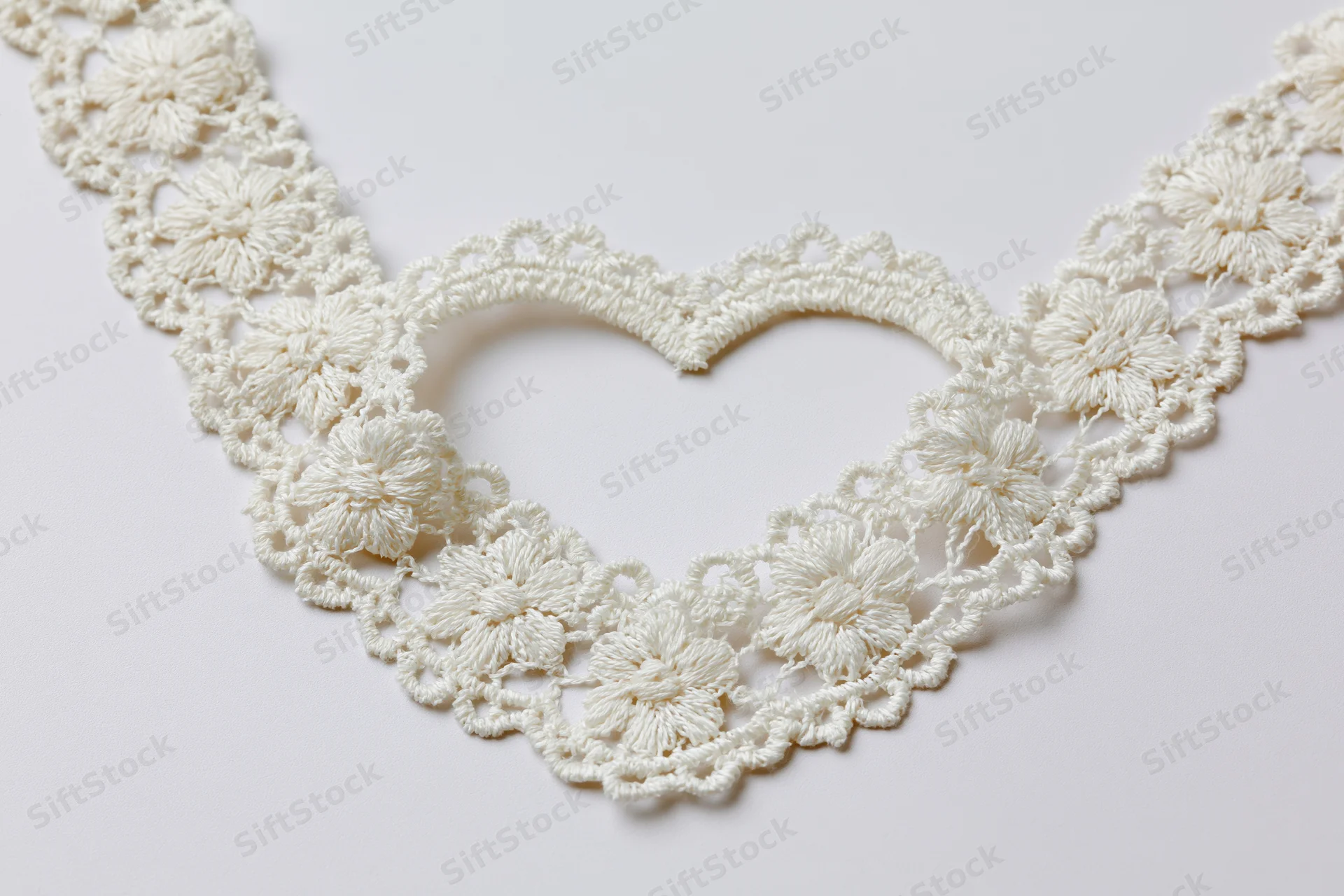 White crocheted lace trim arranged in a heart shape on a plain surface