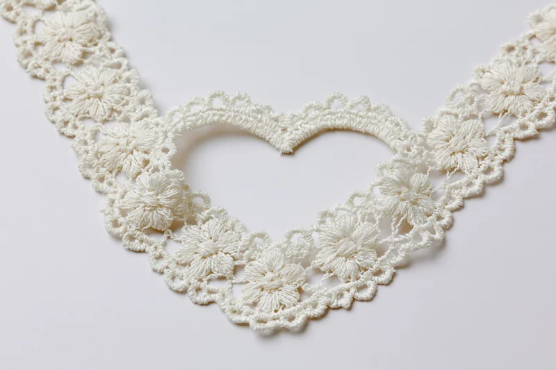 White crocheted lace trim arranged in a heart shape on a plain surface