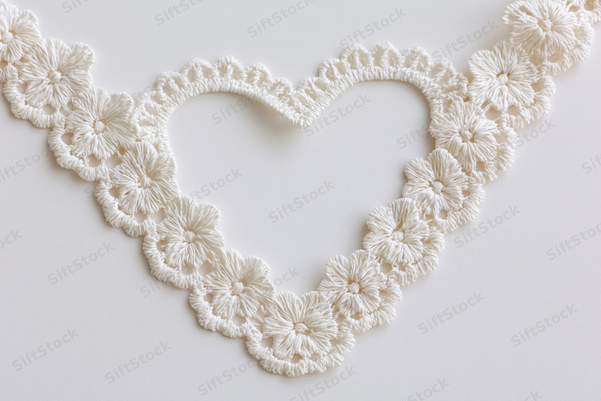 White crocheted lace trim arranged in heart shape on plain surface