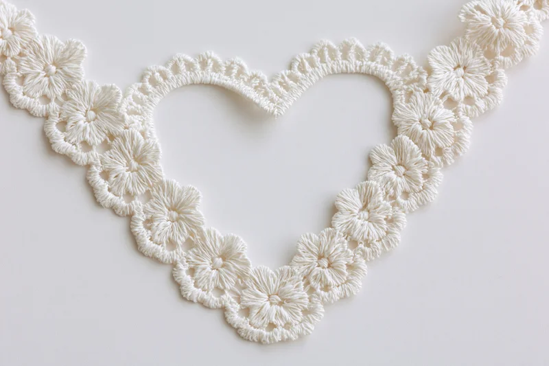 White crocheted lace trim arranged in heart shape on plain surface