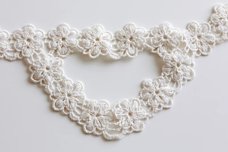 White cotton lace trim arranged in heart shape on plain surface