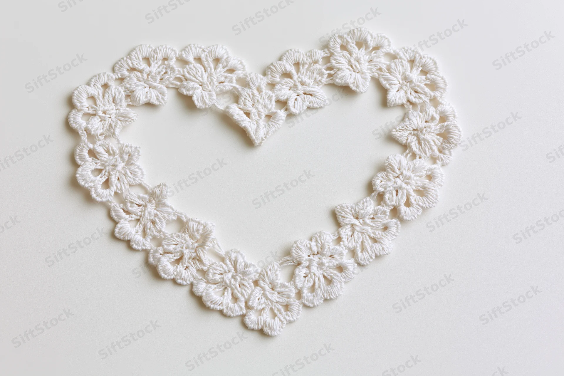 White crocheted lace trim arranged in a heart shape on a plain surface