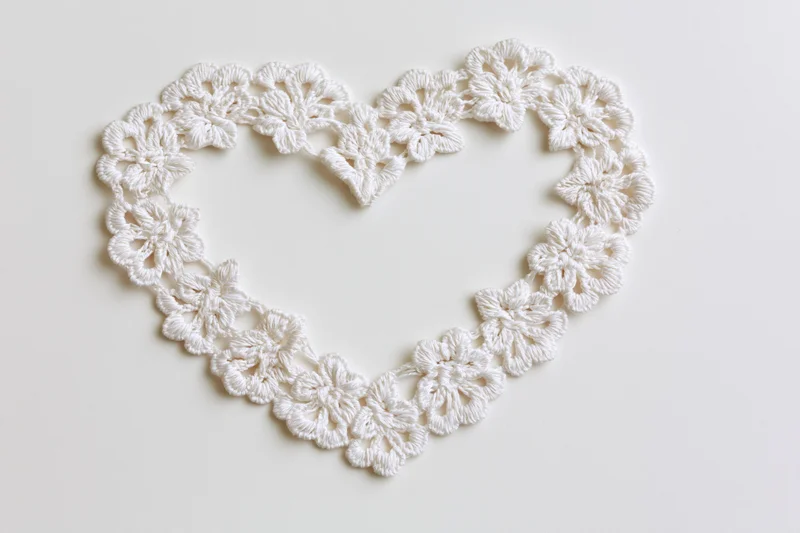 White crocheted lace trim arranged in a heart shape on a plain surface