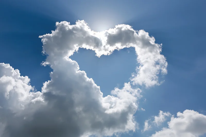 Heart-shaped cloud formation in a bright blue sky with sun shining through