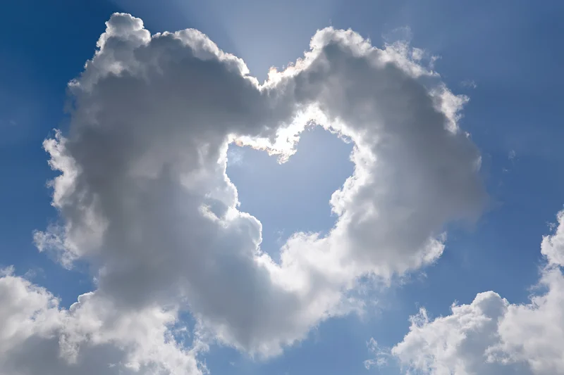 Heart-shaped cloud formation in a blue sky with sunlight shining through