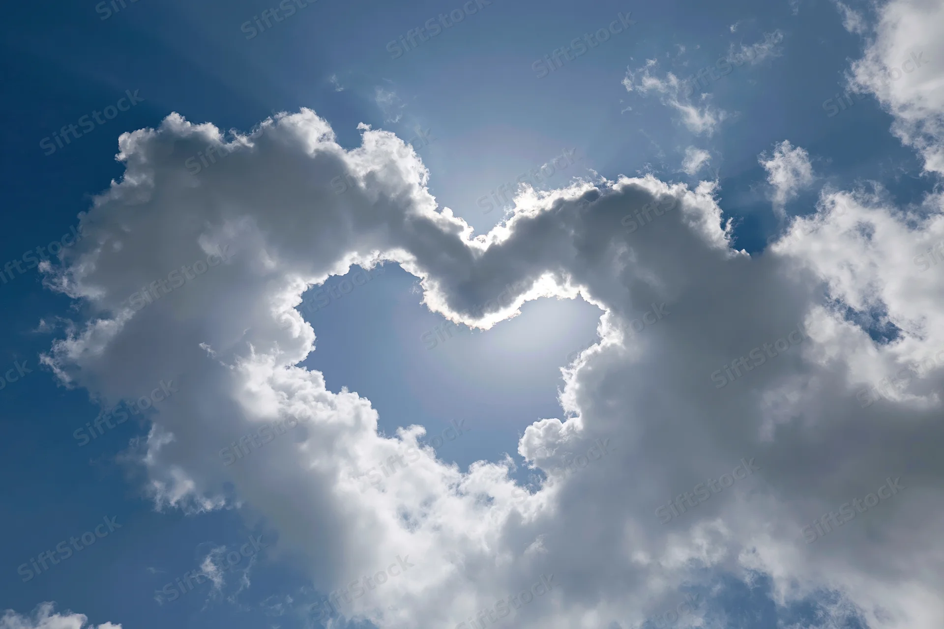 Heart-shaped cloud formation in a blue sky with sunlight shining through