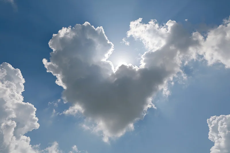 Heart-shaped cloud formation in a bright blue sky with sun shining through