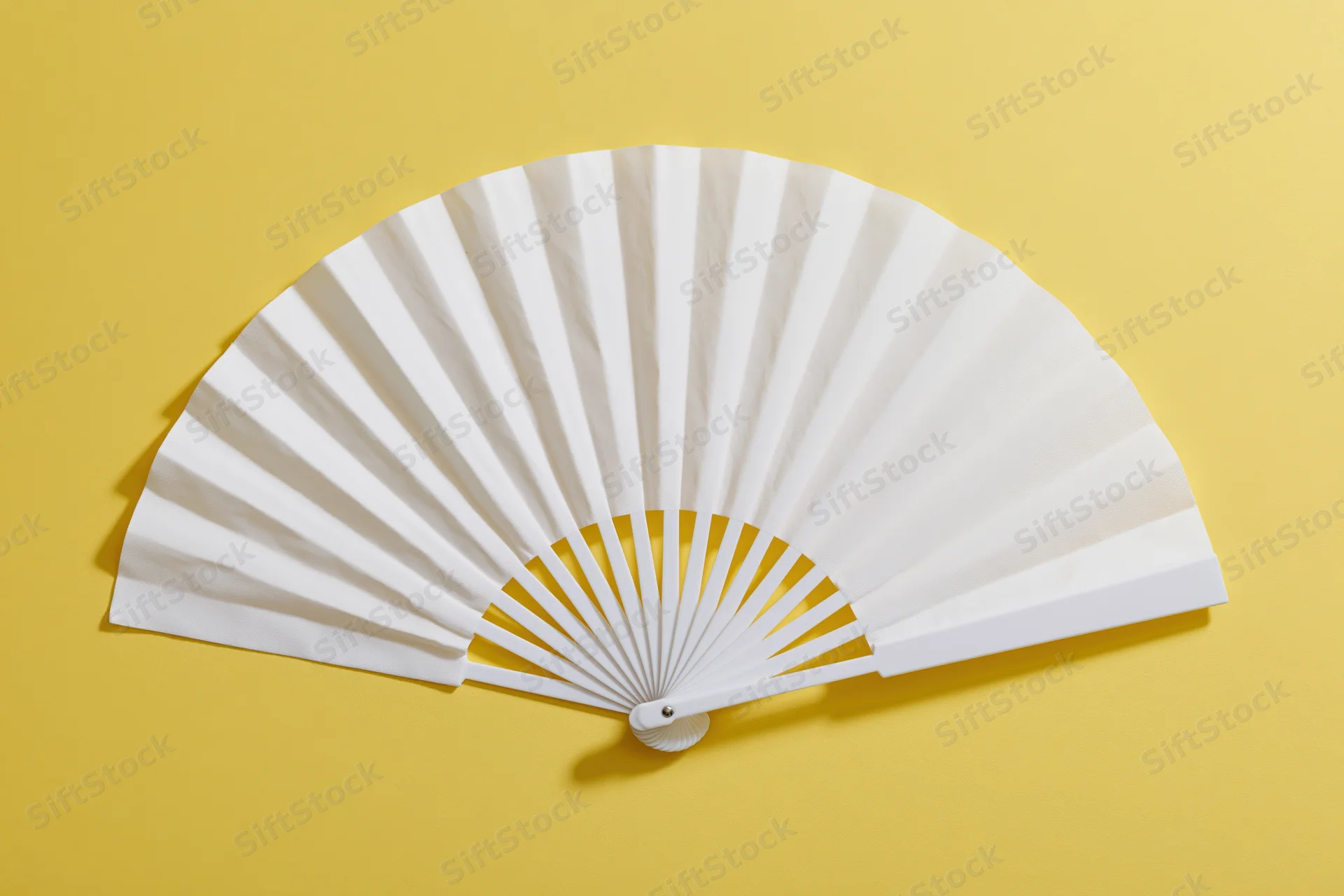 White folding hand fan fully opened and laid flat on yellow background