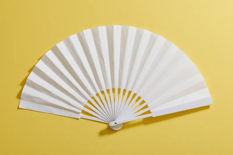 White folding hand fan fully opened and laid flat on yellow background