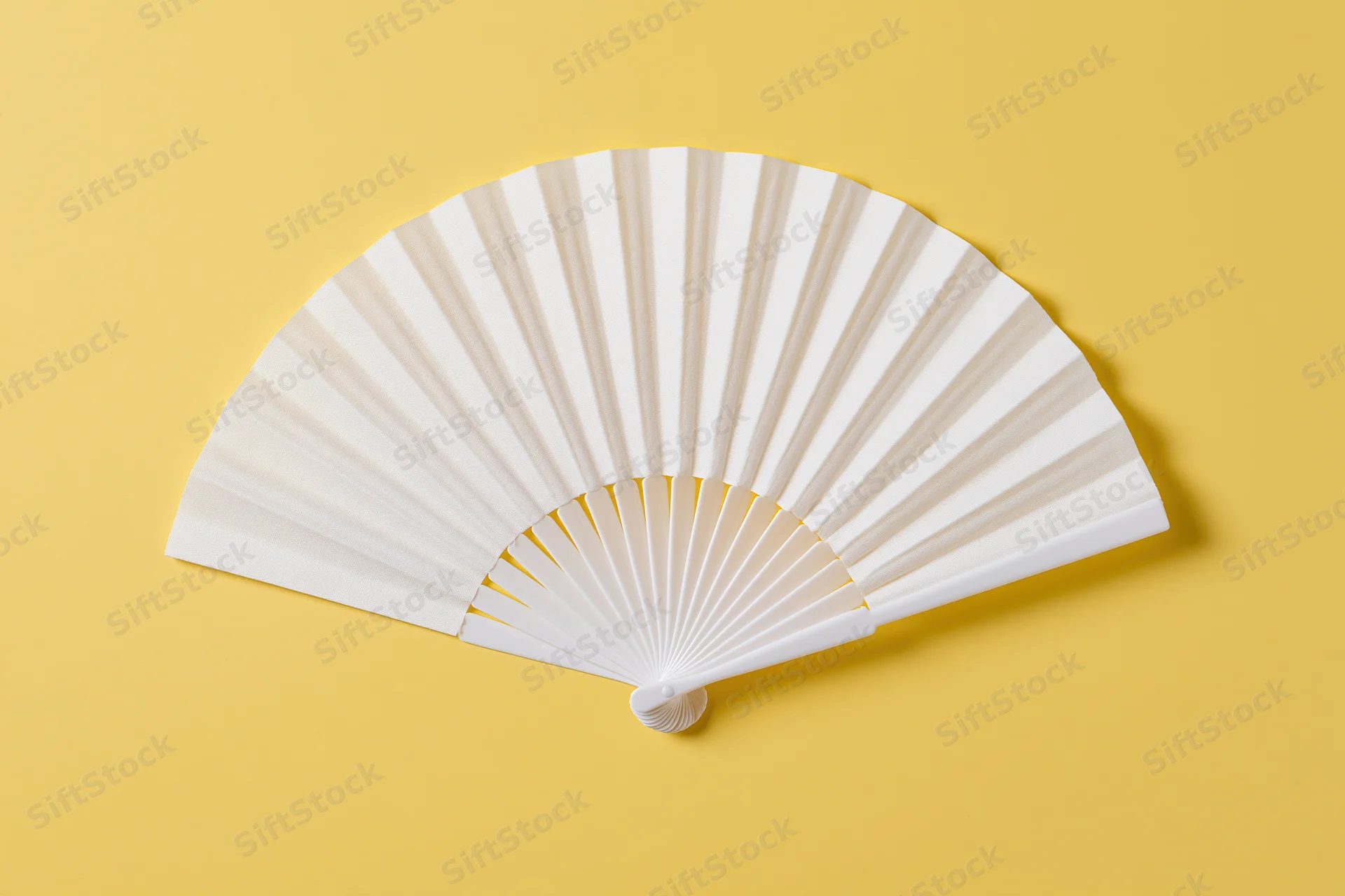 White folding hand fan fully opened and laid flat on yellow background