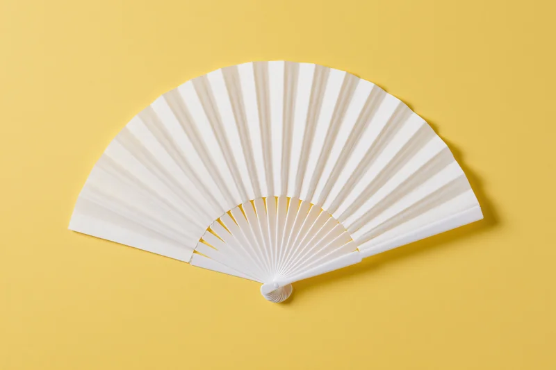 White folding hand fan fully opened and laid flat on yellow background