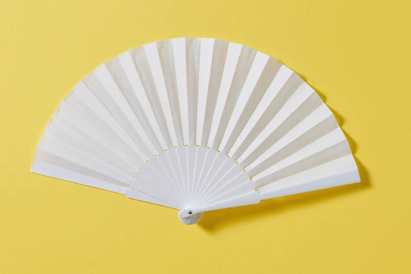 White folding hand fan fully opened and laid flat on yellow background