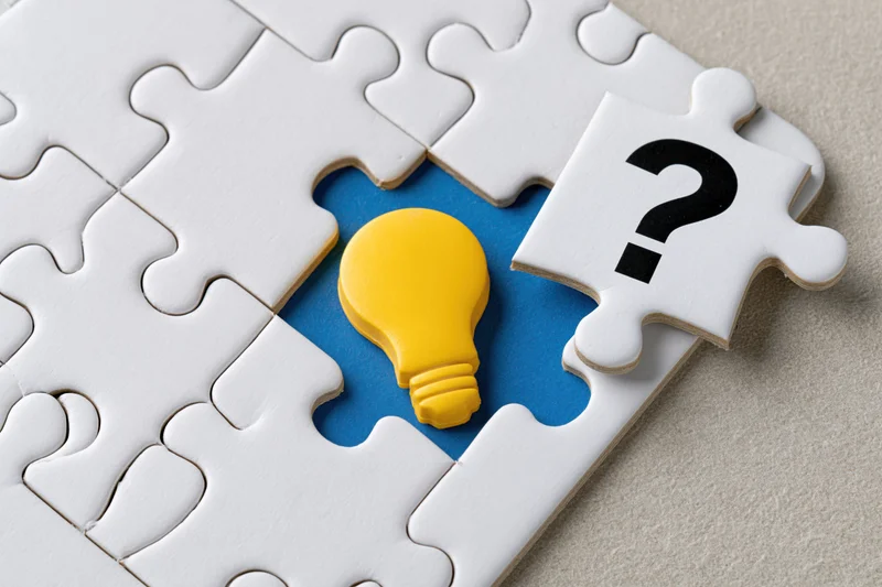 White jigsaw puzzle with one missing piece showing a yellow lightbulb and a question mark on a blue background