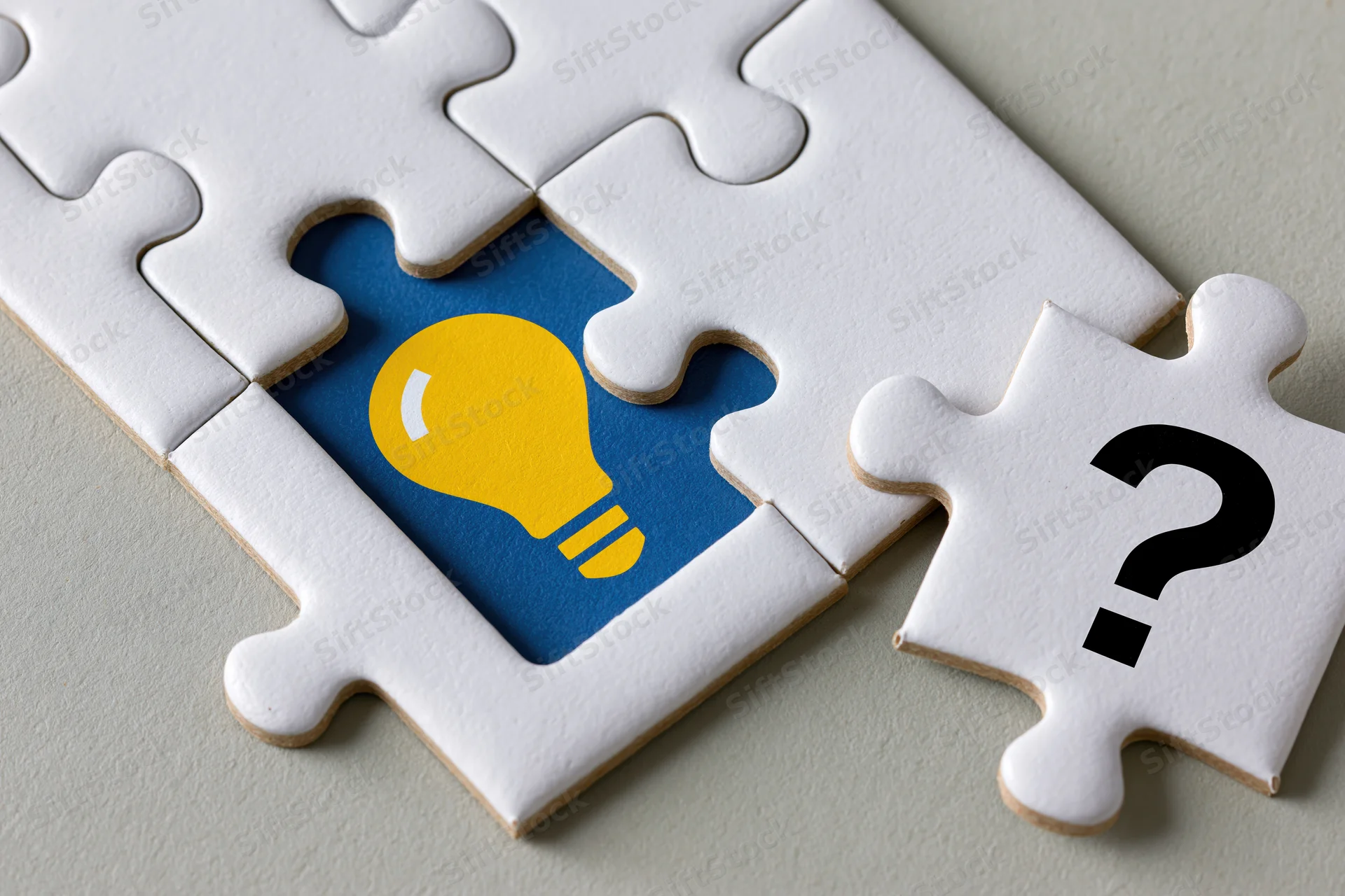 White jigsaw puzzle with missing piece revealing yellow lightbulb on blue background, one piece with question mark beside it