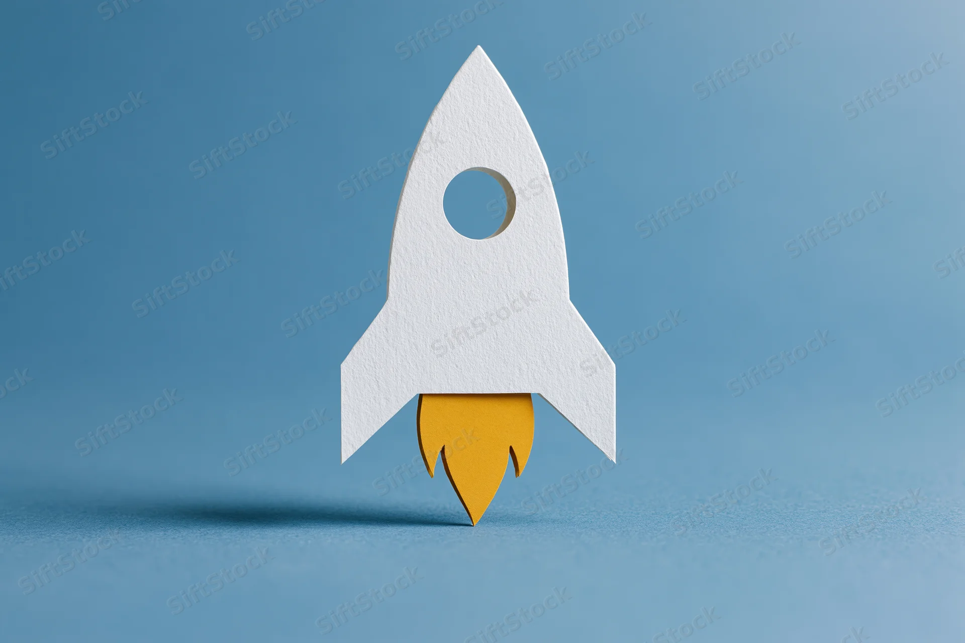 White paper-cut rocket with yellow flame cutout on blue background