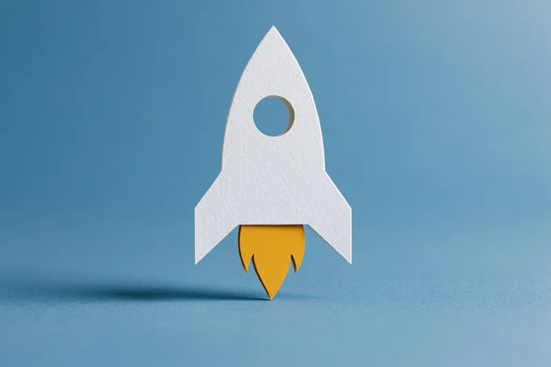 White paper-cut rocket with yellow flame cutout on blue background