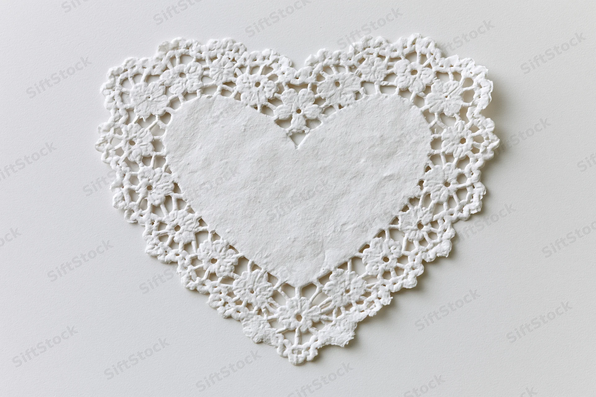 White lace heart-shaped doily lying flat on a plain surface