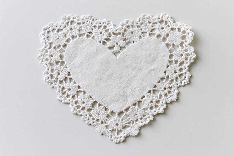 White lace heart-shaped doily lying flat on a plain surface