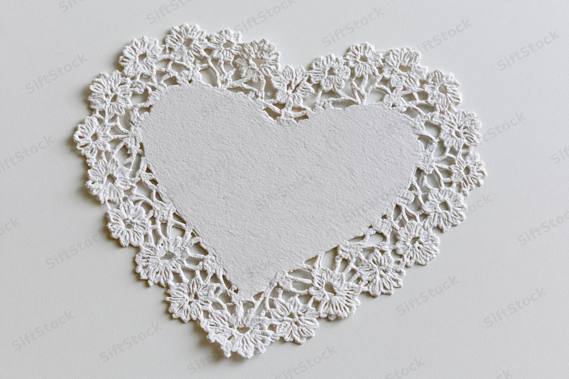 White lace doily cut into heart shape lying flat on light surface