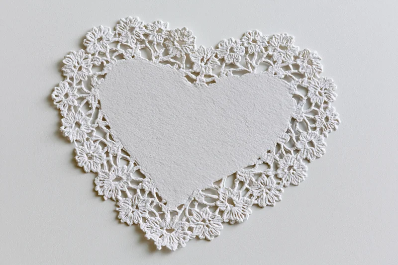 White lace doily cut into heart shape lying flat on light surface