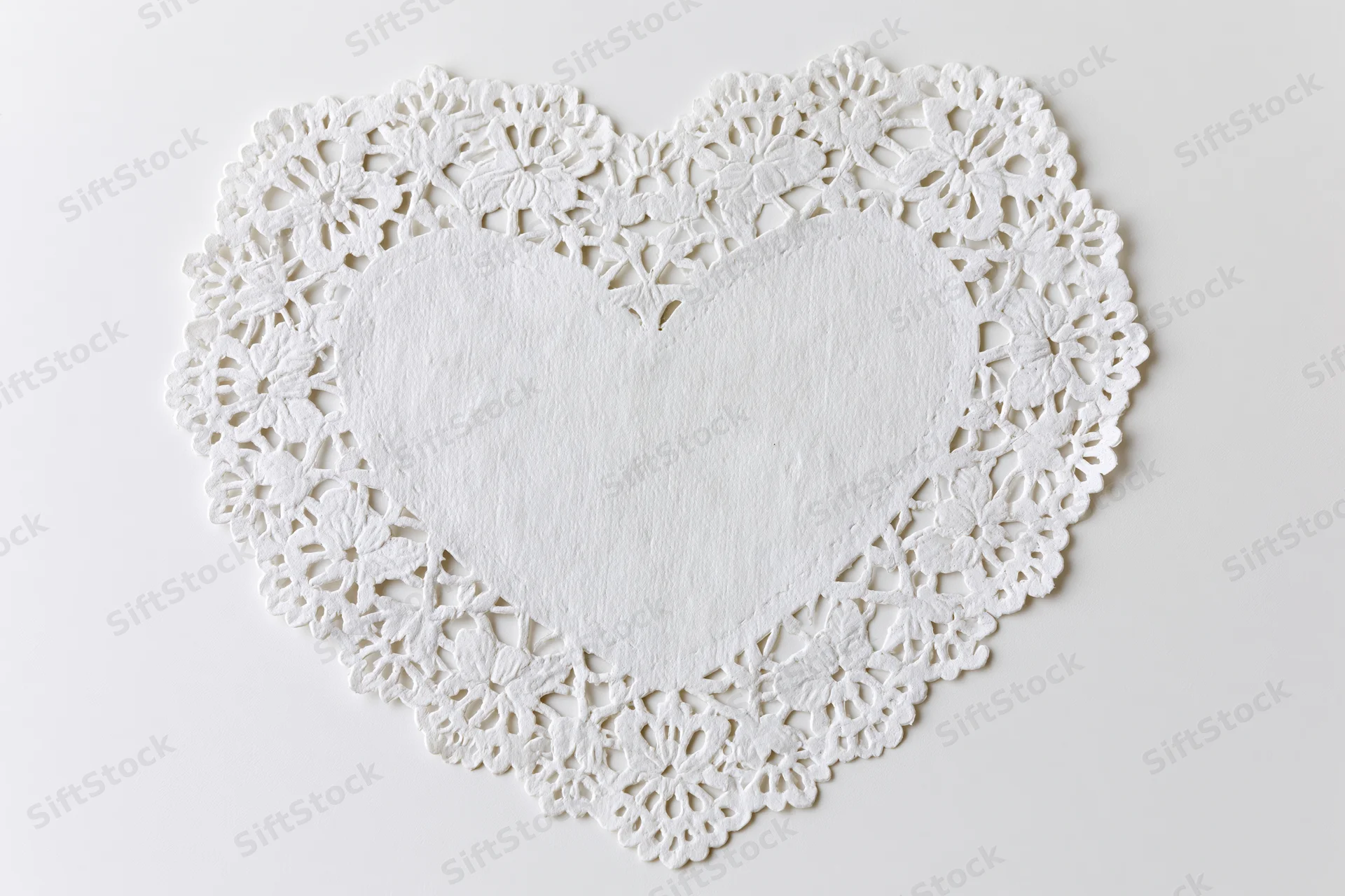 White lace paper doily shaped like a heart lying flat on a plain surface