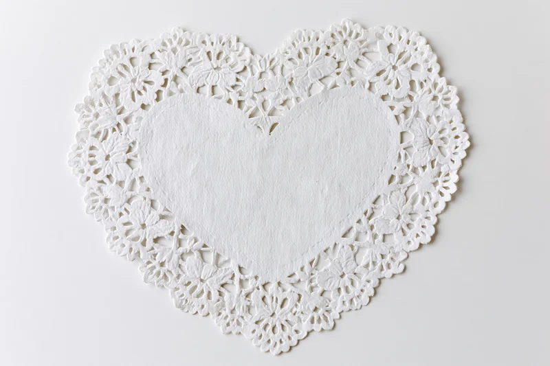 White lace paper doily shaped like a heart lying flat on a plain surface