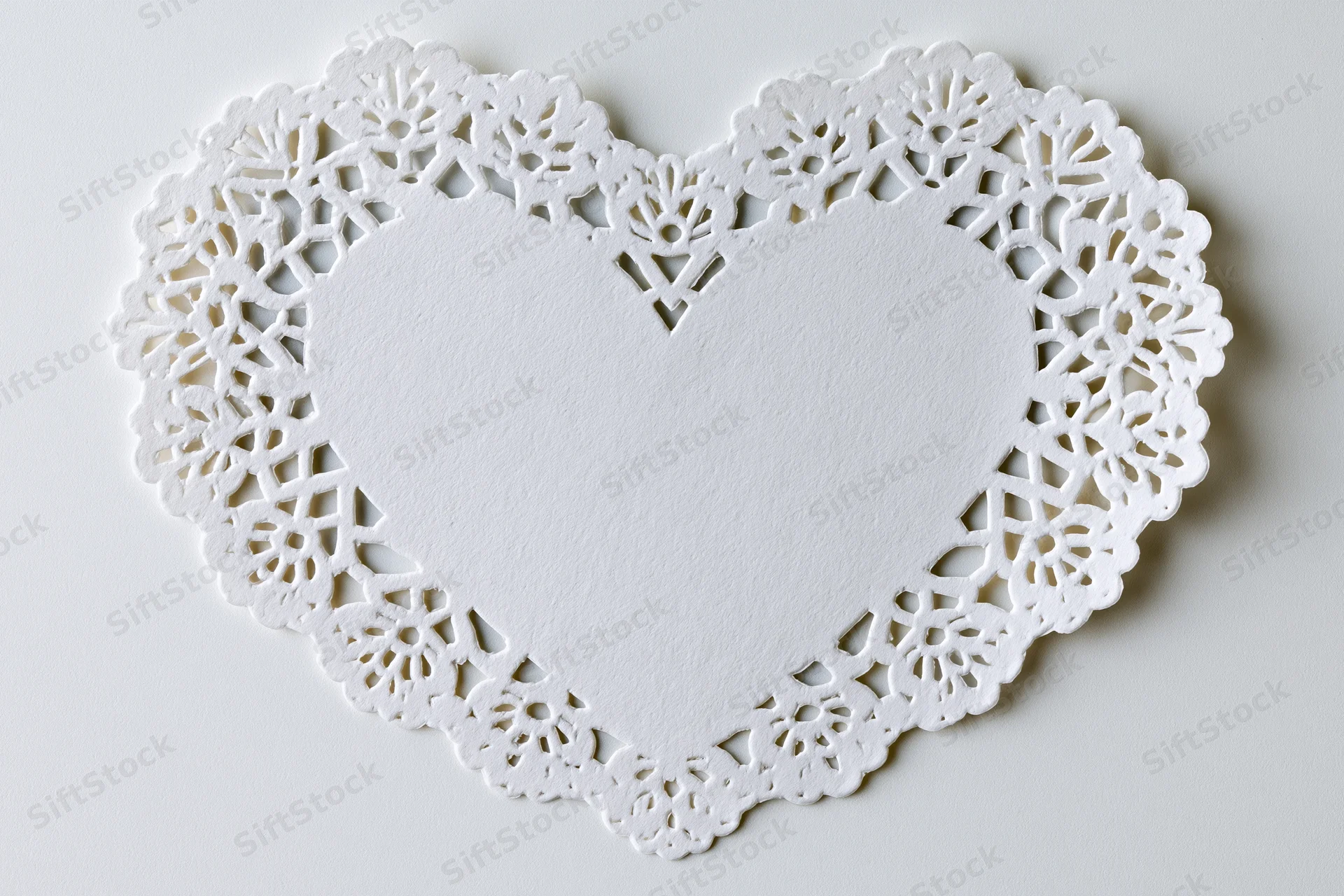 White lace paper doily shaped like a heart lying flat on a plain surface