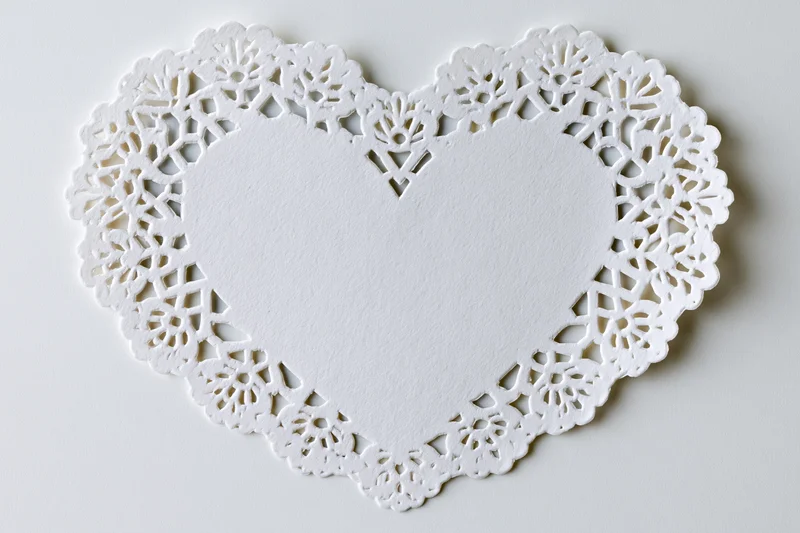 White lace paper doily shaped like a heart lying flat on a plain surface