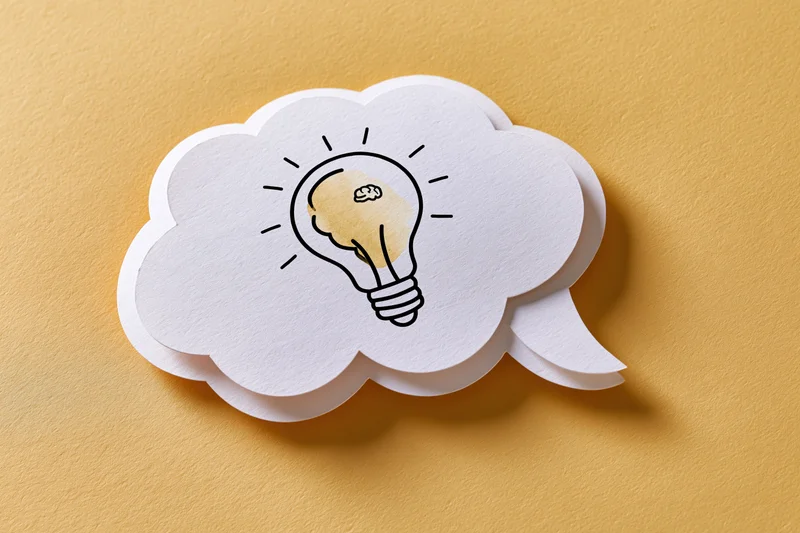 White paper thought bubble cutout with hand-drawn lightbulb on yellow background