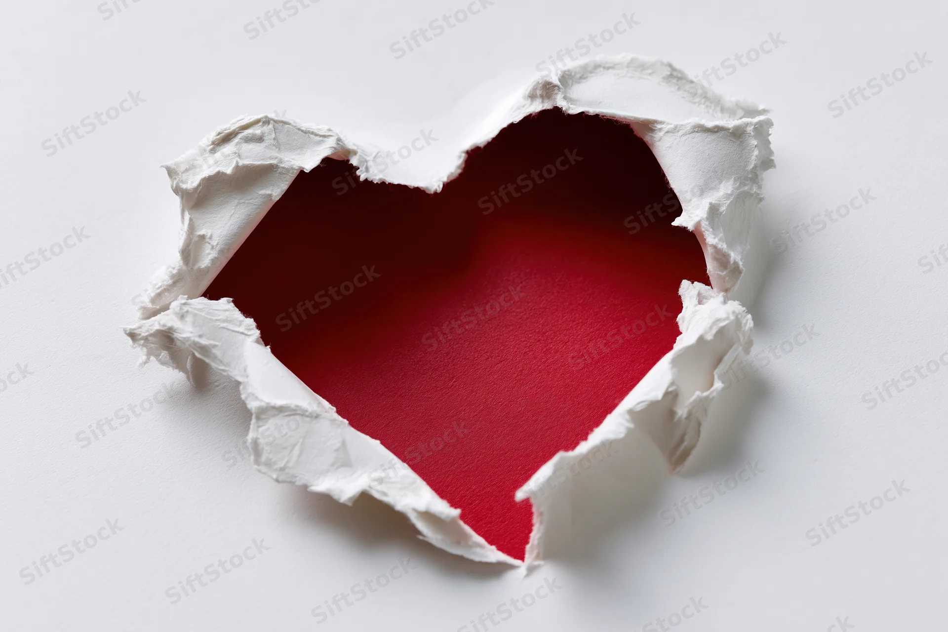 Torn white paper revealing red heart shape on plain surface
