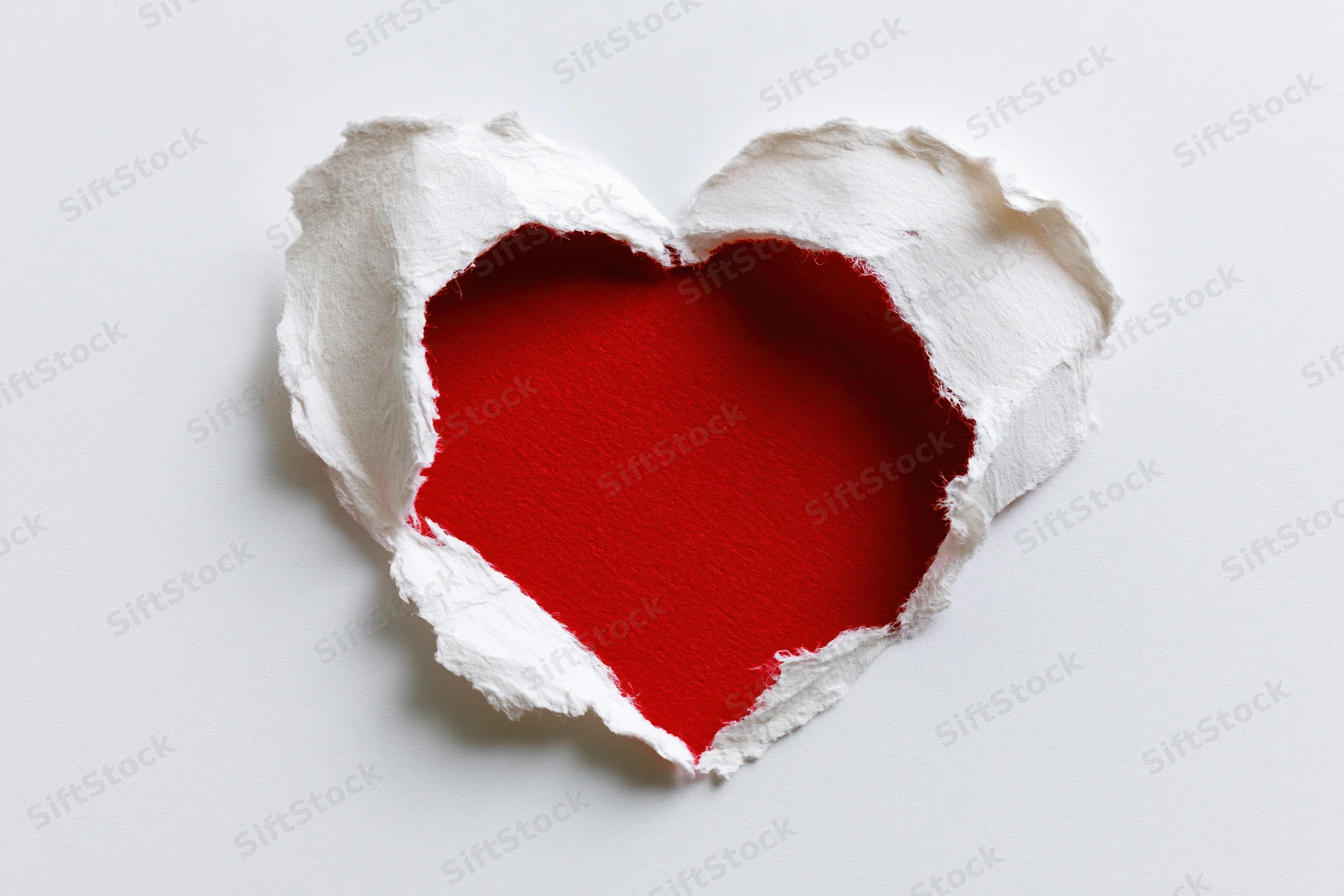 Torn white paper revealing red heart shape on plain surface