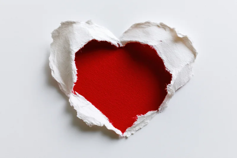 Torn white paper revealing red heart shape on plain surface
