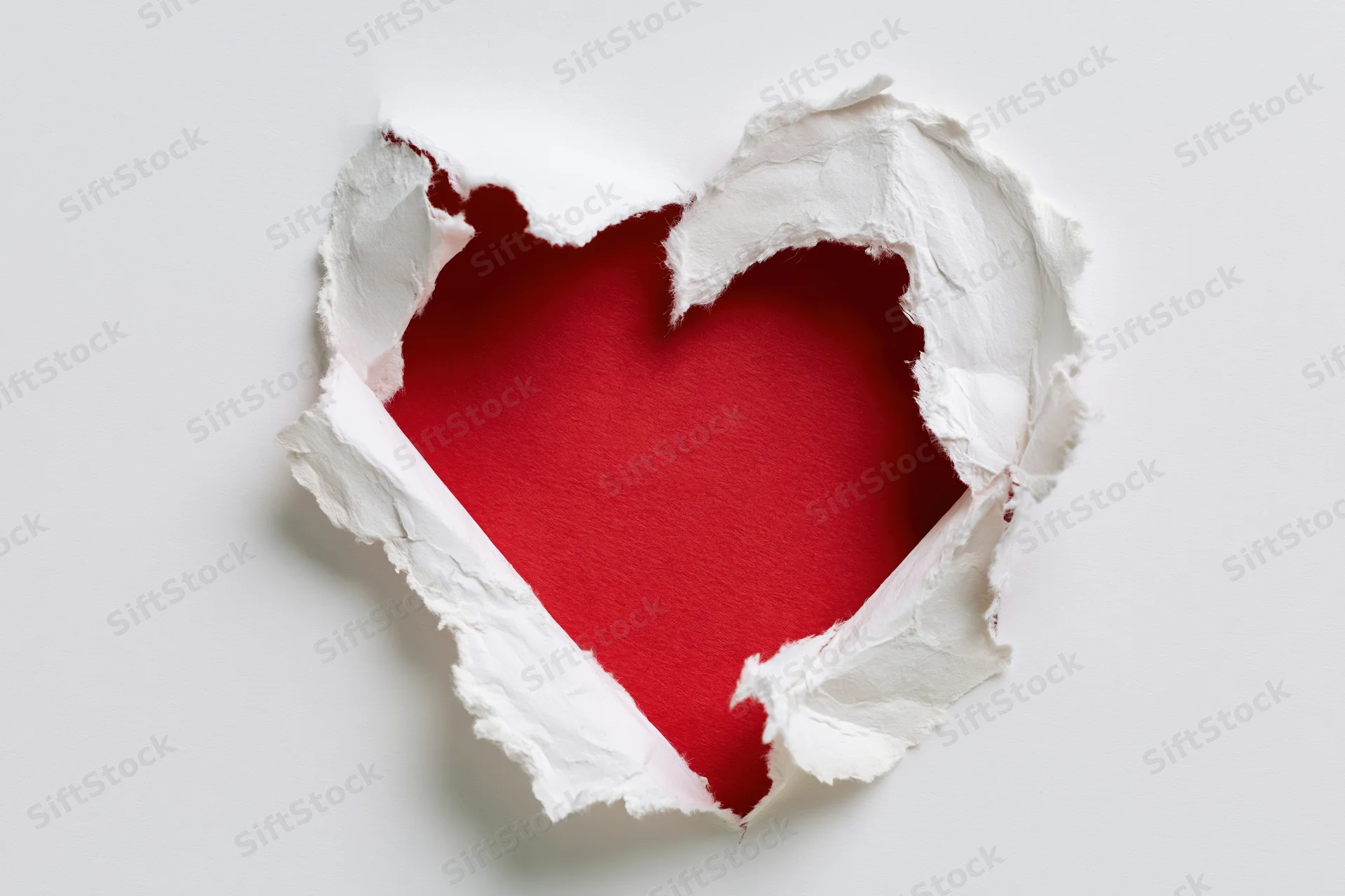 Torn white paper revealing a red heart shape on a plain background