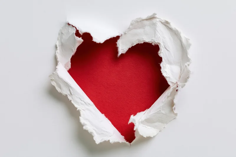 Torn white paper revealing a red heart shape on a plain background
