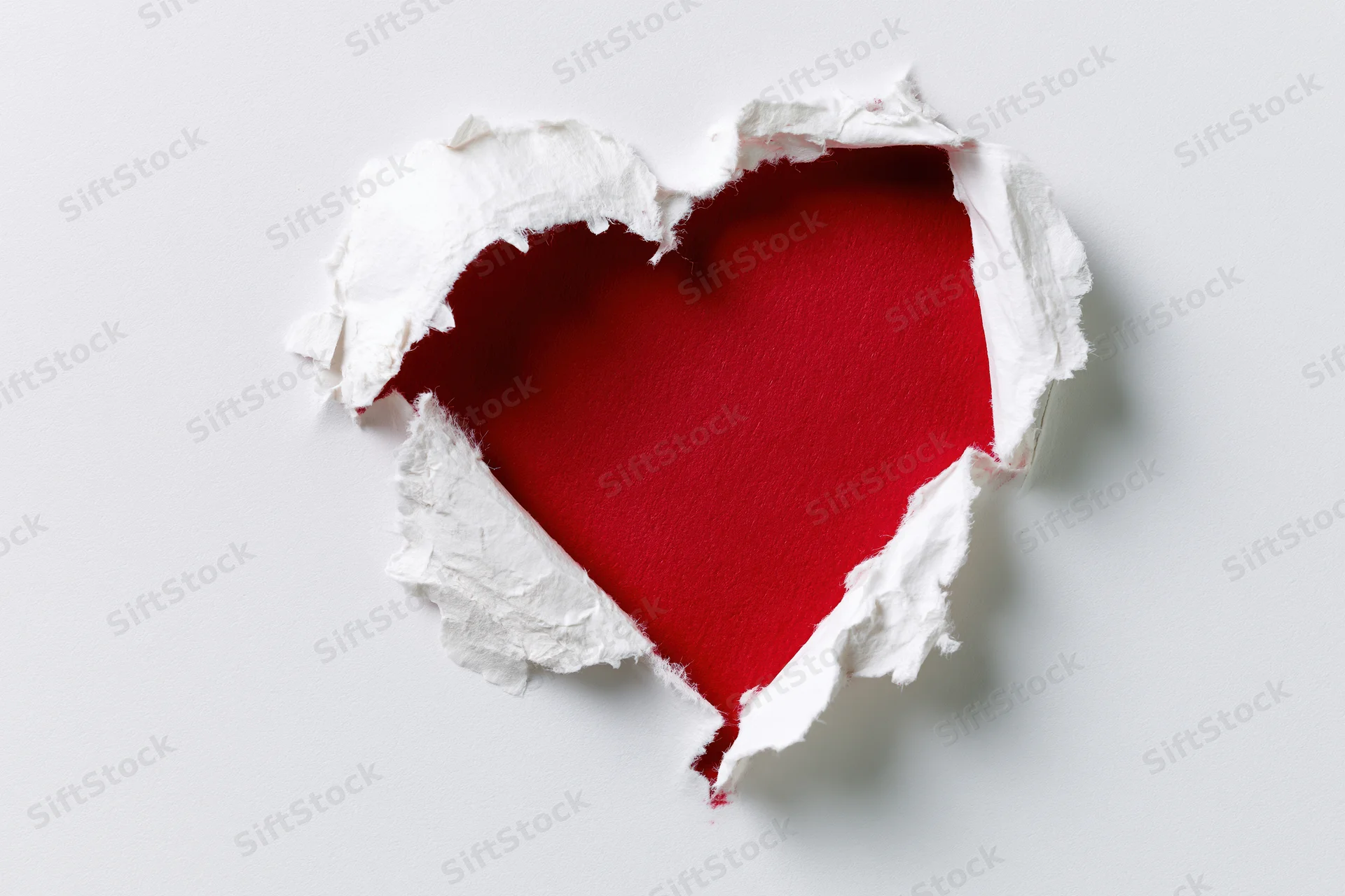 Torn white paper revealing red heart shape on plain background