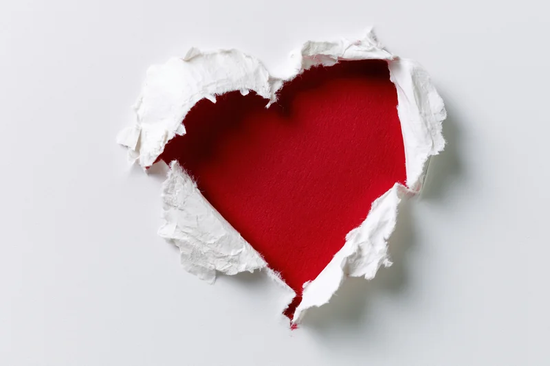 Torn white paper revealing red heart shape on plain background