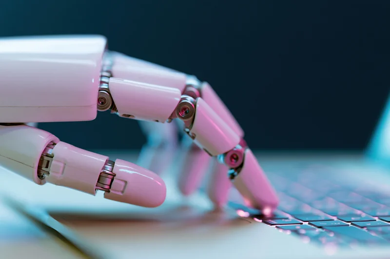 Robotic hand with articulated fingers typing on a laptop keyboard