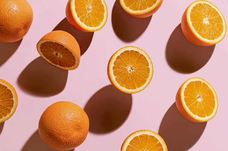Whole and halved oranges arranged in a flat lay on a pink background