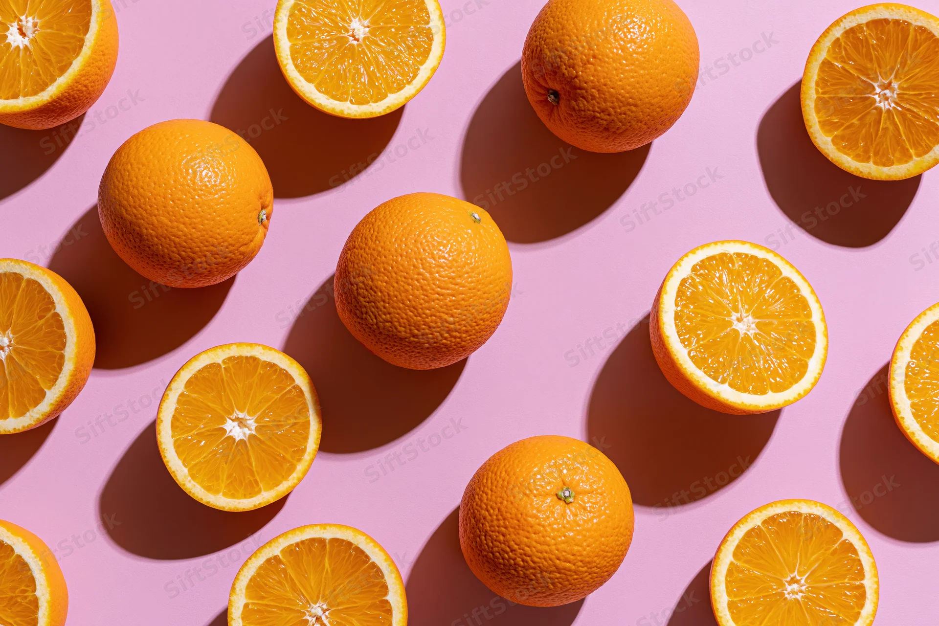 Whole and halved oranges arranged on a pink surface in a flat lay composition