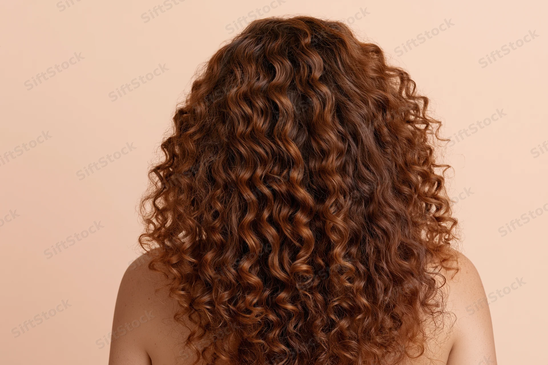 Woman seen from back with long voluminous auburn curly hair against beige background