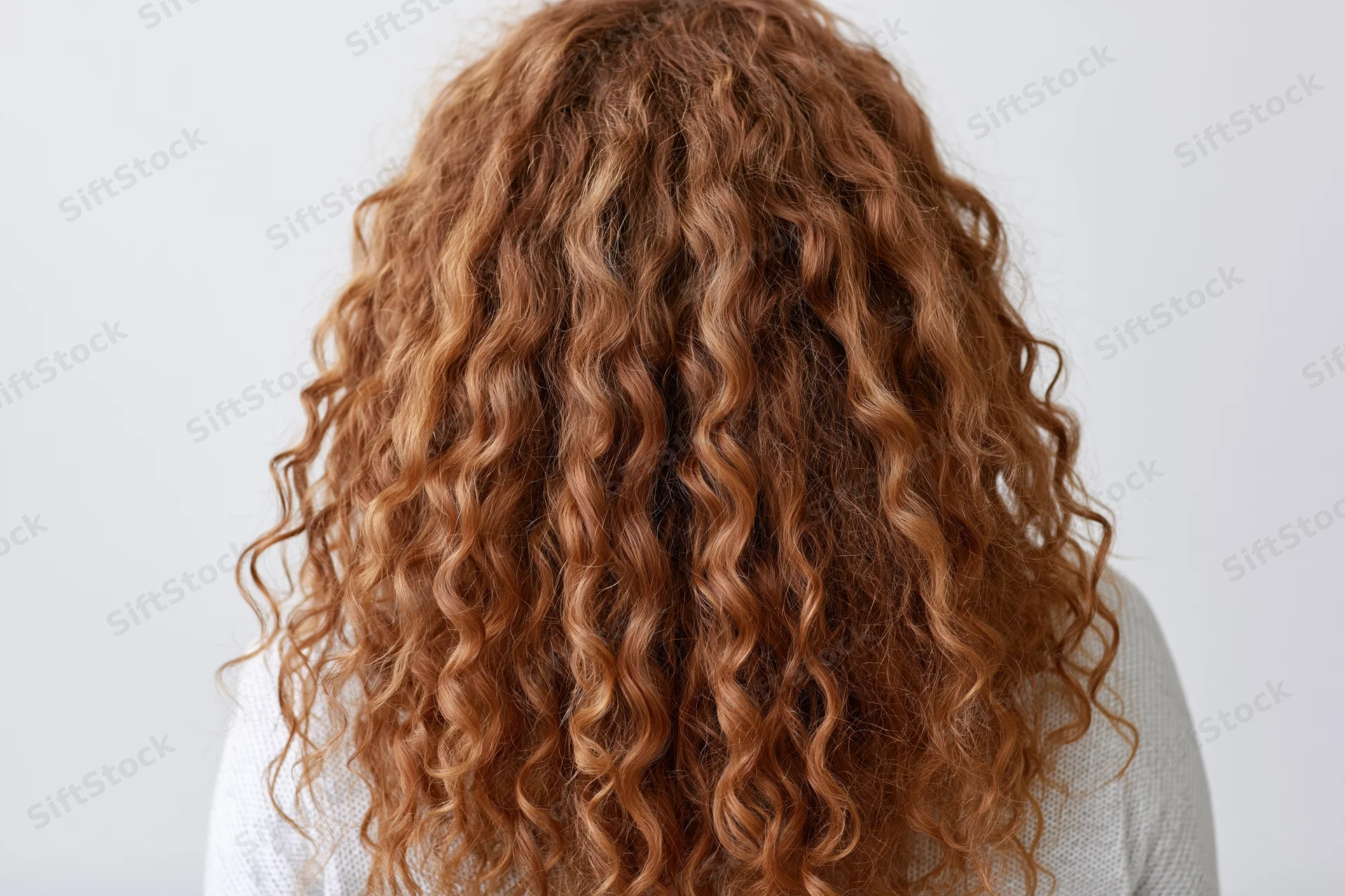 Woman with long voluminous curly red hair seen from back against white background