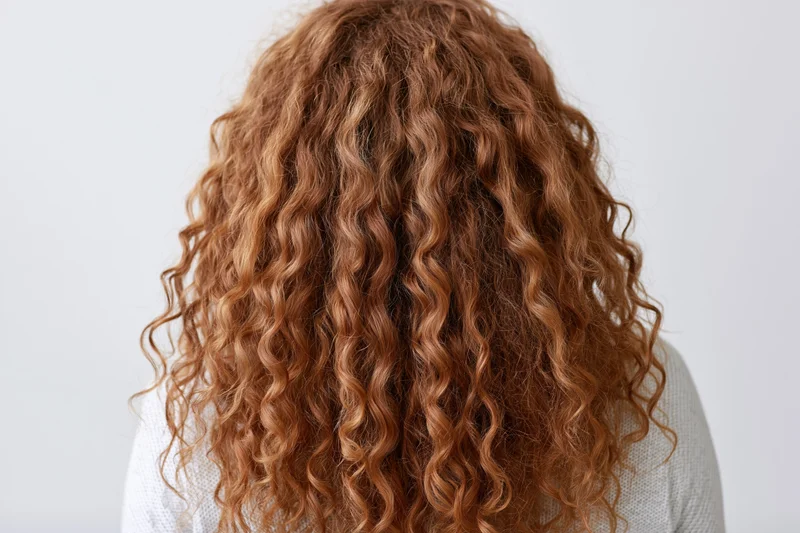 Woman with long voluminous curly red hair seen from back against white background