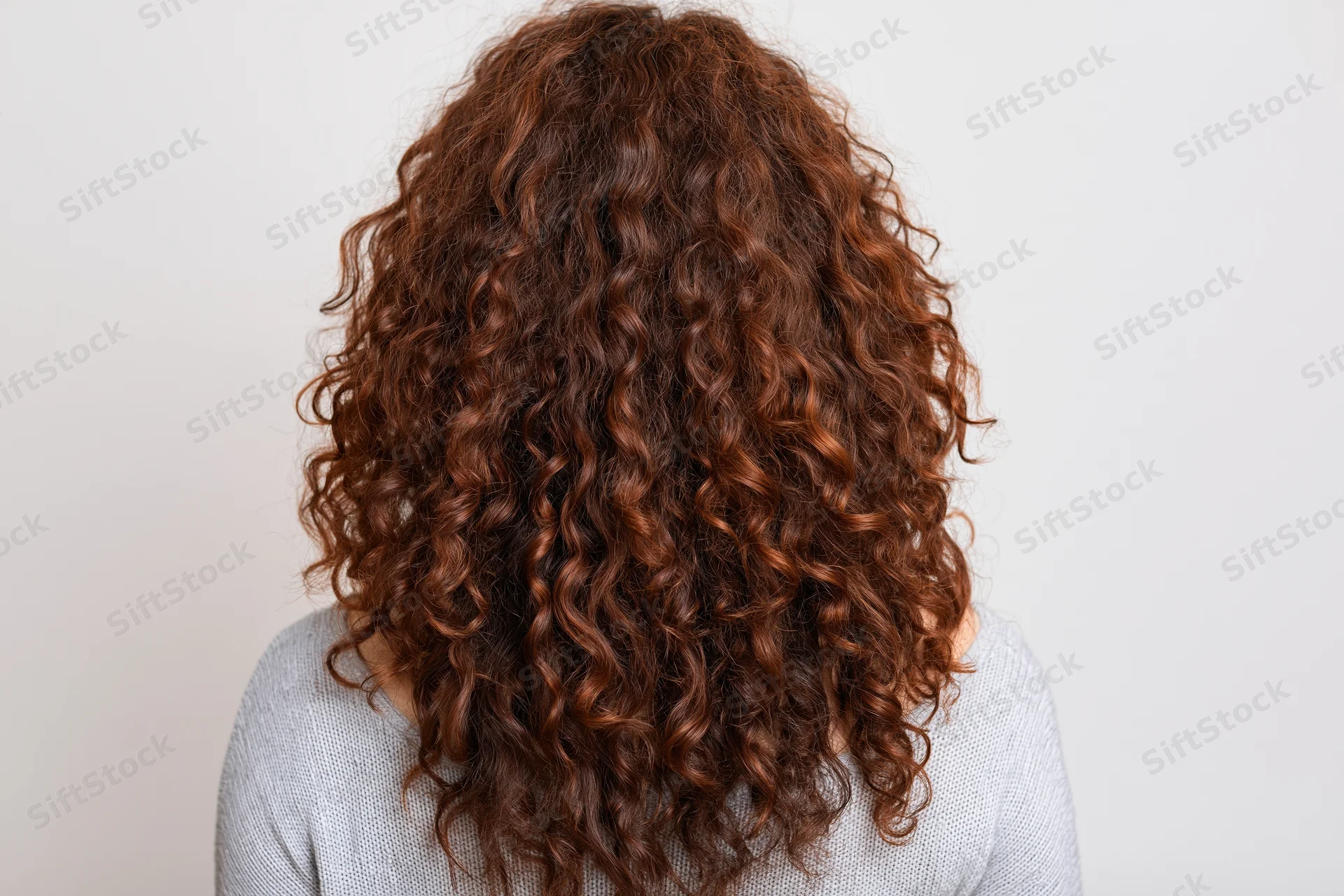 Woman seen from back with long voluminous curly brown hair filling frame