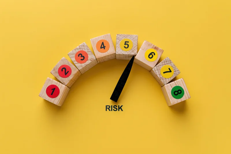 Wooden blocks arranged in semicircle with numbers and pointer indicating risk level on yellow background