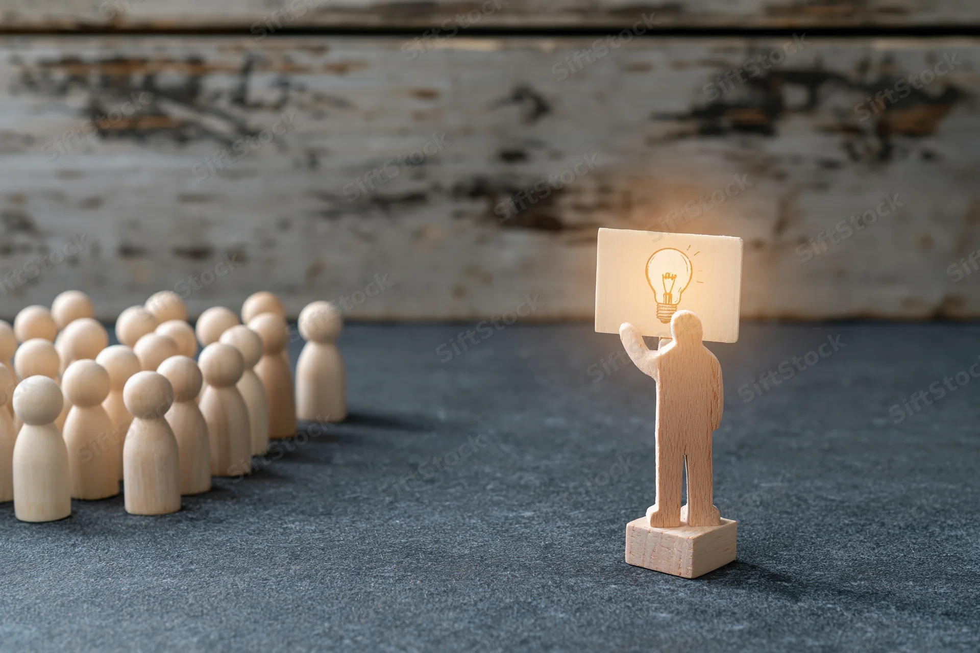 Wooden figurine holding glowing lightbulb sign facing a group of identical figures on textured surface