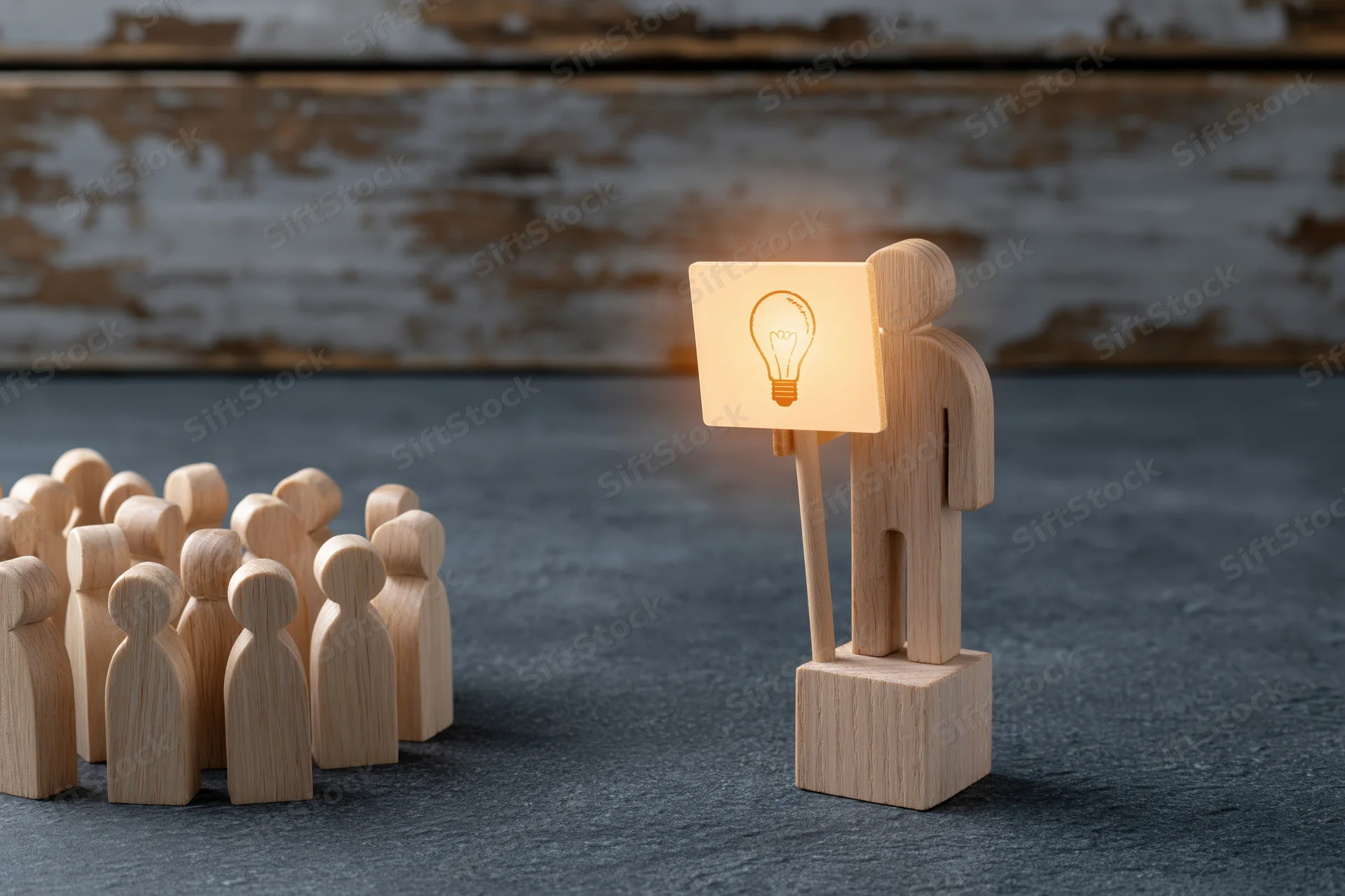 Wooden figurine holding glowing lightbulb sign stands before group of similar figures on dark surface